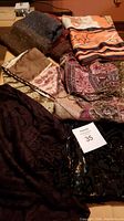 Six assorted scarves and shawls laid out on a surface showing different patterns and colors including brown, metallic gold, and orangish equestrian print.