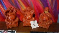 Front view of three red plaster/chalkware sages with different hand poses, on display against colorful background