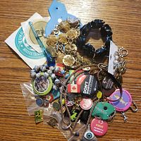 Overview of the mixed lot showing various pins, buttons, bracelets, chains, keychains, and a blue hair clip arranged on a wooden surface.