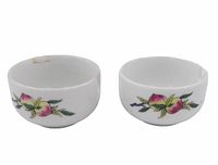 Pair of white porcelain sauce cups with peach fruit and leaf design, each with a pouring spout. One cup has light brown staining near rim.