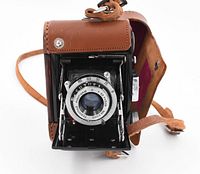 Front view of Baby Suzuka camera showing lens and shutter mechanism inside leather case.