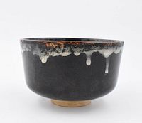Side view of black glazed pottery rice bowl showing white drip glaze and rust highlights