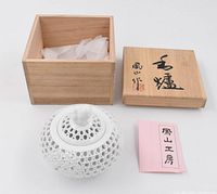 White porcelain bowl with intricate open lattice design and floral relief, lid topped with squirrel figurine, shown alongside wooden box and certificate.