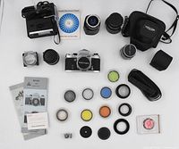 Top-down view showing Miranda Sensomat camera body at center, Vivitar electronic flash unit, multiple lenses, colored lens filters, camera cases, manuals, and various accessories laid out for display.