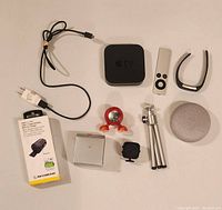 Top view of all items in lot including Apple TV box with remote, Fitbit, Google Home Mini, chargers, tripod, and device holder.