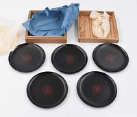Five black handmade wooden Japanese coasters with red circular pattern, two square wooden boxes (one with blue cloth lining, one with cream cloth) displayed on white background.