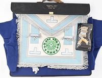 Photo showing the masonic lambskin apron laid out with embroidered emblem patches and silver jewel bars, alongside the black travel case.