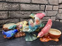 View of the five vintage ceramic bird planters and figurines arranged on a dark surface against a brick wall showing colors and overall condition.
