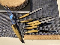Photo showing six knives and one carver fork from Crown Sheffield laid on table with ruler for size reference, displaying horn-colored handles and stainless steel blades