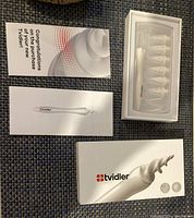 Photo of Tvidler ear wax cleaner kit including device, replacement tips in plastic case, instruction manuals, and packaging box.