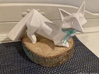 White geometric ceramic fox figurine placed on rustic round wood base with bark edges on a blue textured surface in front of white painted furniture.