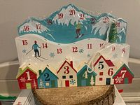Wooden advent calendar showing colorful numbered houses and snowy mountain design with 24 days for countdown