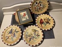 Top view showing four Lenox Winter Greetings plates with different bird designs and a framed Cardinal woven art print.