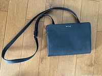 Front view of black Matt and Nat crossbody purse with adjustable strap on wooden floor.