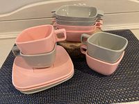 Full view of stacked pastel pink and grey melamine cups, saucers, and bowls showing the full retro set.