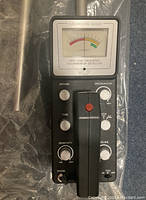 Close-up of the main control unit of the metal detector showing the analog meter, control knobs and handle.