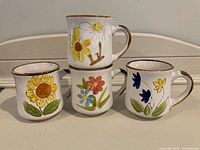 Four mid-century ceramic mugs stacked and displayed showing different floral hand-painted designs and brown trim