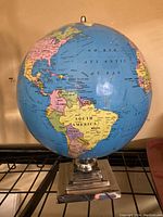 Photo of a world globe showing the Americas front and center, mounted on a modern silver tone metal base with a stepped square design.