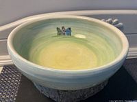 Front angle showing round shape and house motif painted inside bowl with blended mint green, blue, and yellow glaze.