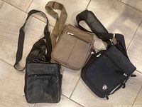 Photo of three crossbody purses, one brown leather and two black fabric, laid flat showing front and strap details.