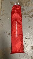 Red nylon carrying bag with Rawlings logo on floor, containing folded soccer practice net and frame.