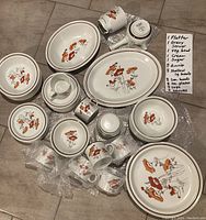 Overview of the 61-piece Royal Doulton Lambethware Field Flower pattern dinnerware laid out, showing platters, bowls, cups, saucers, cream and sugar containers, and a gravy ladle server with a note listing item counts.