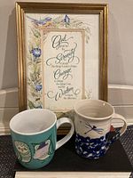 Framed Serenity Prayer print with two porcelain mugs marked by owl and blue dragonfly designs