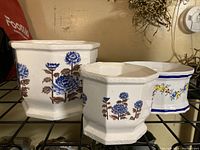 Three ceramic planters of different sizes: two hexagonal with blue and brown flowers, one rectangular with a blue and yellow floral pattern and blue trim