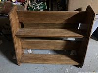 Front view of wooden book stand showing three horizontal shelves and angled side panels.