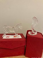 Two clear glass figurines, a horse and a cobra snake, positioned on and beside red gift boxes.