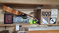 Wide view of lot items including toy guitar, two boxed Boost Oxygen cannisters, framed insect, and small miscellaneous items on shelf.