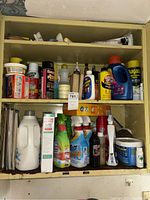 Full view of cabinet shelves containing an assortment of cleaning supplies, sprays, cans, and bottles.