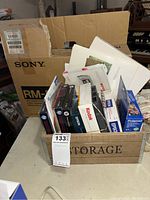 Box labeled Sony RM-4 with wooden crate labeled STORAGE containing assorted photo papers and tapes from Kodak, Epson, Polaroid, HP.
