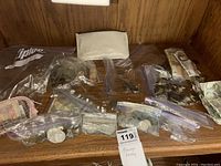 Wide view of all currency items including multiple plastic bags with coins, paper currency, and small pouches on a wooden surface.