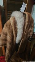 Front view showing the brown fur jacket with contrasting white fur collar hanging on a wooden chair.
