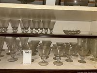 Wide view of multiple frosted drinking glasses and goblets arranged on shelves, showing approx 50 pieces with rounded clear glass stem detail