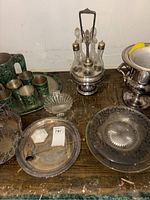 Photo showing assortment of silver-tone serving platters, condiment set, and a silver bucket.