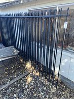 Black metal wrought iron fencing panels with pointed tops leaning against an outdoor wall, showing condition and style.