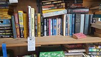 Wooden shelf with multiple rows of paperback and some hardcover books, including titles by C.J. Cherryh, John Grisham, and Michael Palmer
