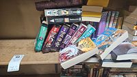 Photo showing array of paperback books on the third shelf including stacks of books by various fantasy and sci-fi authors such as Mercedes Lackey and Anne McCaffrey