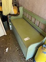 Photo of a green wooden storage bench with backrest and hinged seat storage, side angle showing armrest and storage bin underneath.