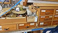 Wooden storage drawers with labeled compartments and miscellaneous items on top, including a straw hat