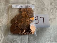 Clear plastic bag labeled "1961 D unc" containing about 37 uncirculated Lincoln Memorial pennies from 1961 Denver mint shown spread and stacked on a table with a paper numerical label 37.