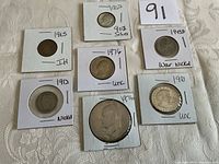 Seven U.S. coins from different years and types, each set in a cardboard holder, displayed on a light fabric background.
