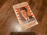 Photo of the John F. Kennedy campaign poster showing the entire front side with clear text and portrait on wooden floor.