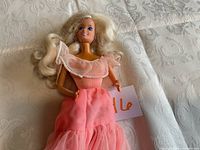 Full body photo of vintage Barbie doll lying down, showing pink multi-layered dress and long blonde hair.