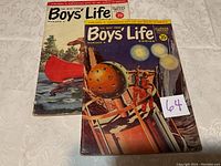 Two Boys' Life comics displayed, number 3 and number 4, positioned on a patterned white cloth background.