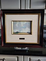 Framed lithograph of a landscape with a cloudy sky and fields, showing Italian Roma moulding black and gold frame.
