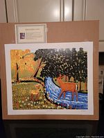 Full view of the unframed Maud Lewis print mounted on brown backing, showing colorful deer and stream scene.