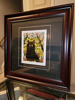 Framed fine art print by Maud Lewis showing a black cat with bright yellow eyes, floral background, signed by Maud Lewis. Print mounted with black matte and dark brown wooden frame.